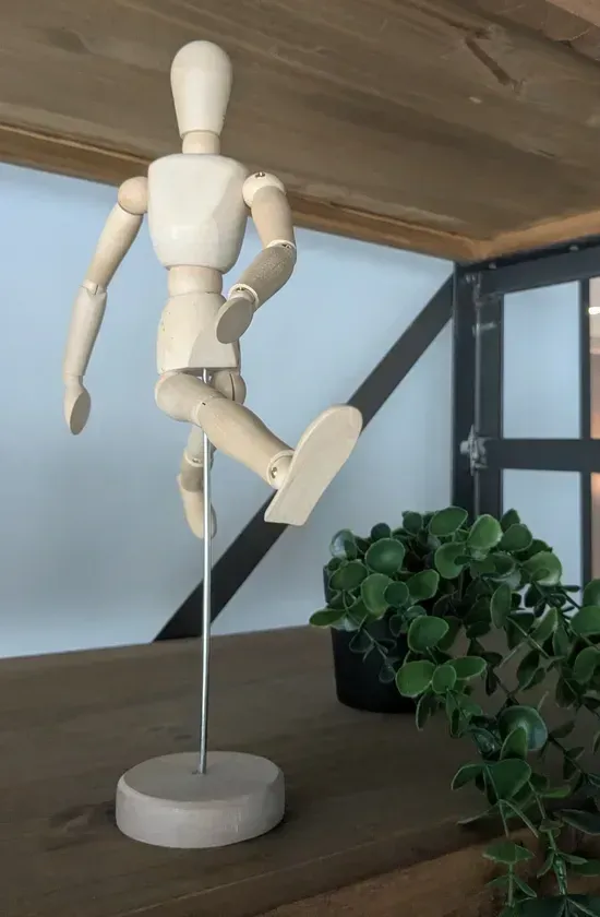photo: wooden humanoid figure in dynamic mid-stride position on stand w/ plant adjacent